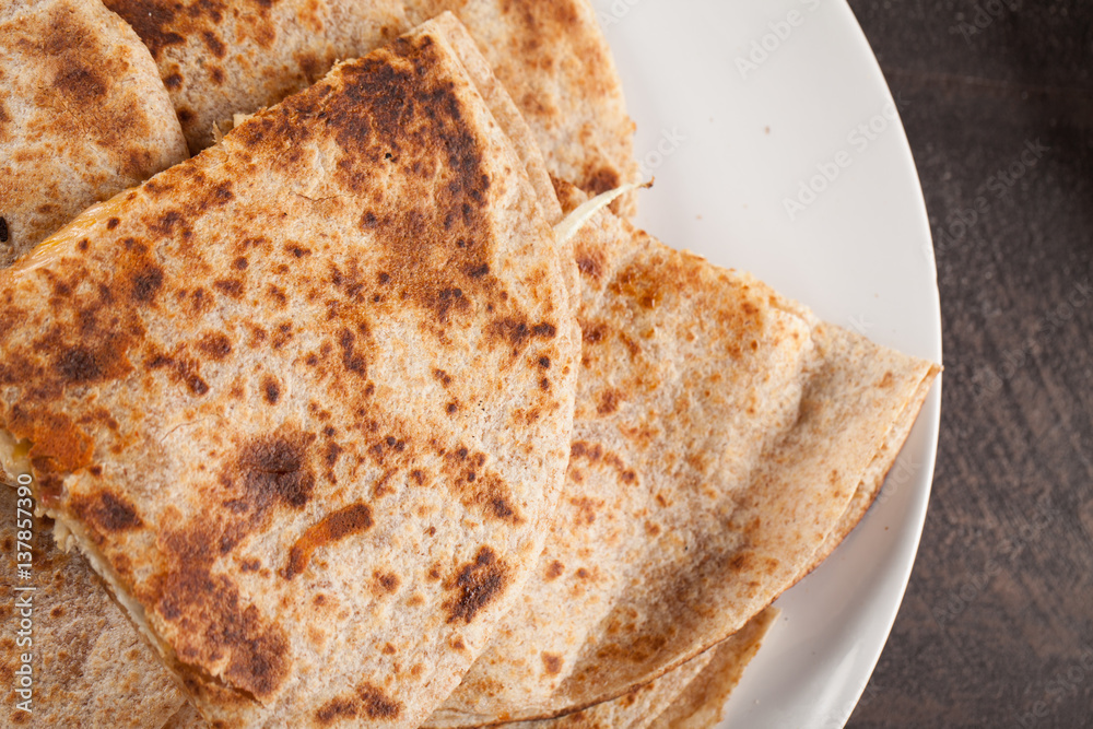 Crispy Quesadilla with Chicken and Sauce on white plate on dark wooden background above shot Crispy Quesadilla with Chicken and Sauce on white plate on dark wooden background above shot