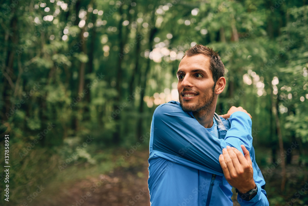Fit male jogger stretches during day training for cross country forest trail race in a nature park. Fit male jogger stretches during day training for cross country forest trail race in a nature park.