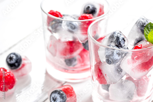 Icecubes with blueberry and raspberry in glass on wooden table