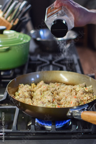Wallpaper Mural man sprinkles salt on fried rice in wok over gas flame stove Torontodigital.ca