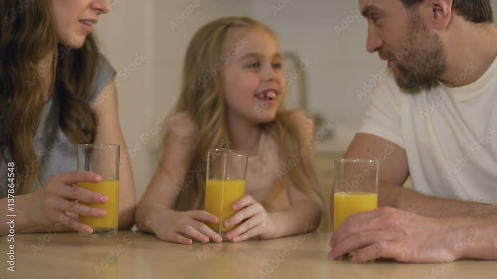Happy healthy family drinking orange juice with smiles on faces, morning at home