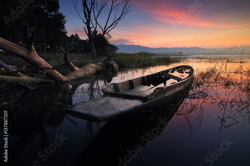 Silhouette beautiful scenery of nature and wreck fishing boats moored beached on the beach during sunrise time and the colorful sky at Bang Pra Reservoir , Chonburi province in Thailand © goodze