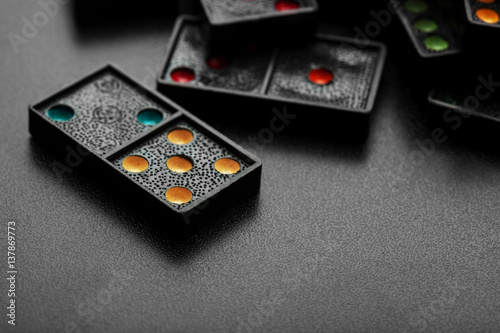 Black color dominoes with colorful dot game pieces lying on dark background