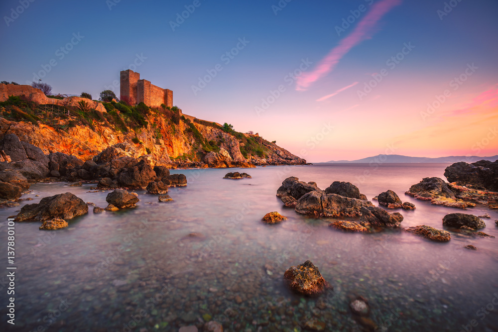 Talamone rock beach and medieval fortress at sunset. Maremma Argentario, Tuscany, Italy
