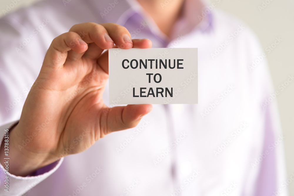 Businessman holding a card with text CONTINUE TO LEARN Businessman holding a card with text CONTINUE TO LEARN