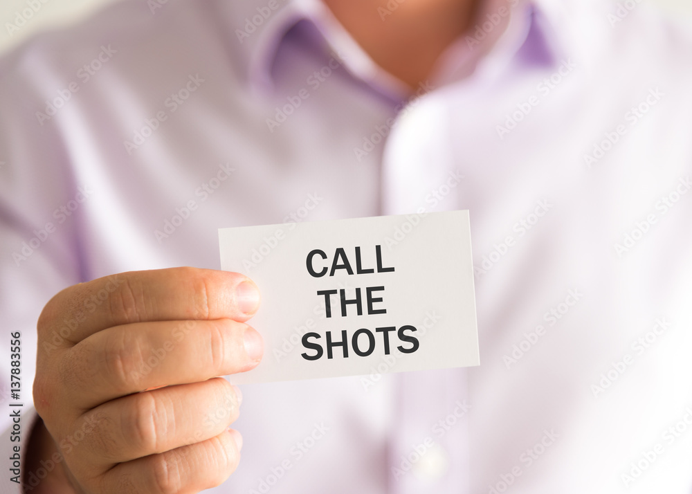 Businessman holding a card with text CALL THE SHOTS Businessman holding a card with text CALL THE SHOTS