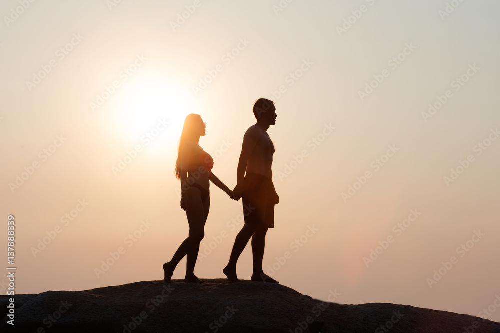 Lovely young adult couple walking on the rocks above tropical sea in Sunset.