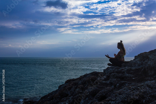Silhouette of woman meditating near the ocean. Side view of female meditating near the sea. Horizontal outdoors shot.