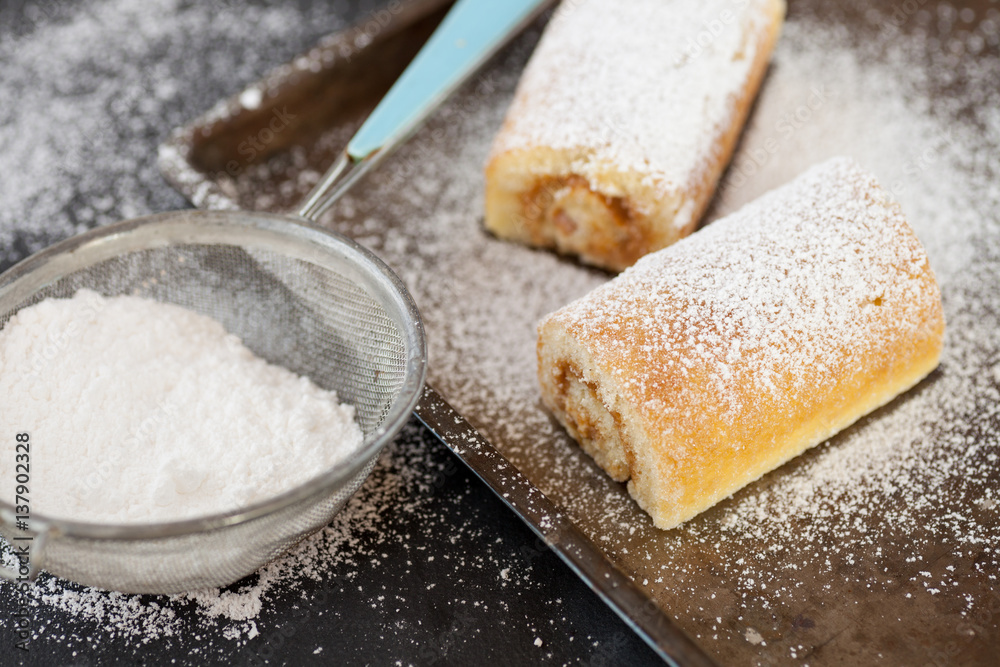 Swiss rolls on baking tray with sieve and icing sugar
