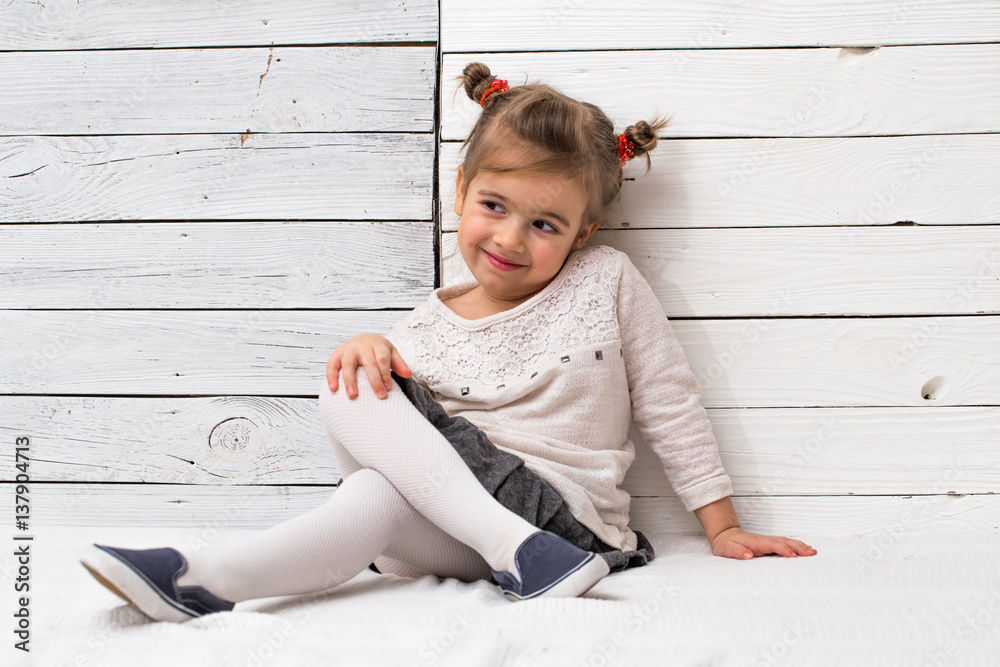 Naklejka premium little cute girl school girl sitting on white wooden background