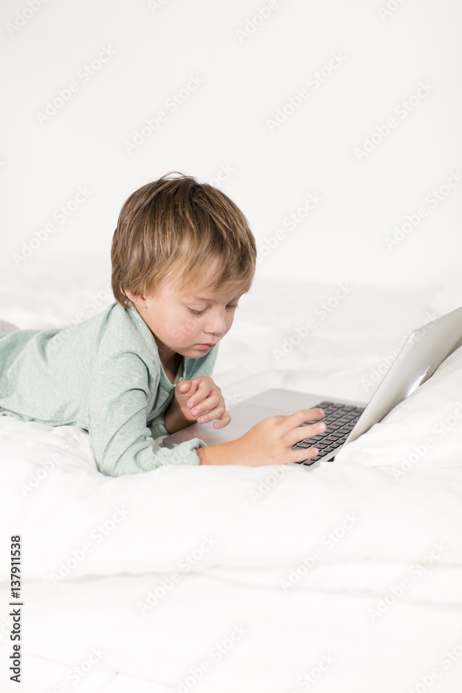 Ein Junge mit Notebook liegt auf einem Bett Ein Junge mit Notebook liegt auf einem Bett