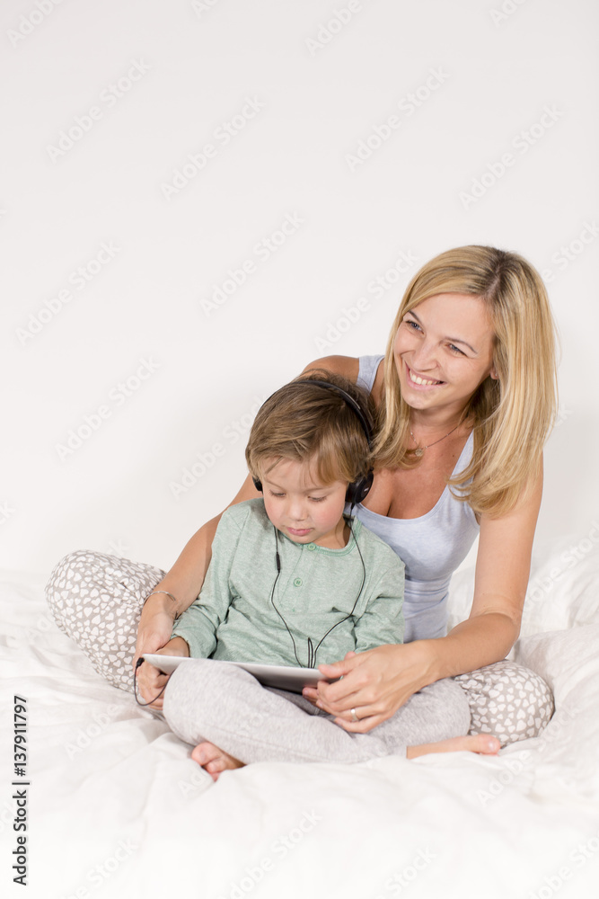 Mutter und Sohn sitzen mit tablet und Kopfhörer auf einem Bett Mutter und Sohn sitzen mit tablet und Kopfhörer auf einem Bett