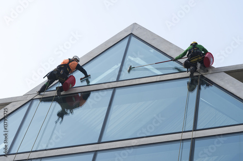Window washers cleaning the glass facade of a modern building, high risk work. photo