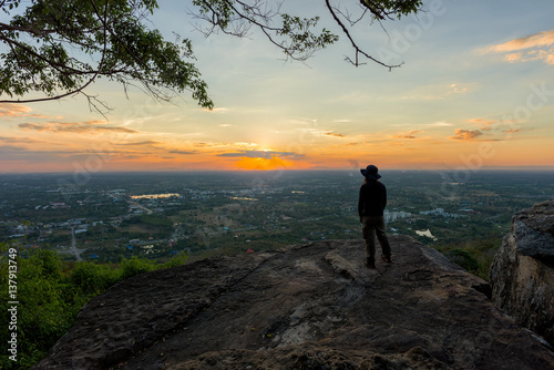 Young man traveler on cliff with beautiful landscape sunset over cliff and city