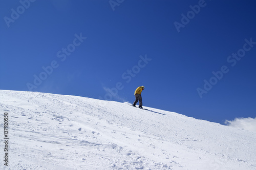 Snowboarder downhill on off-piste slope and blue clear sky