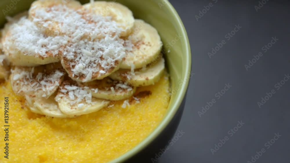 Corn porridge with banana, coconut and cinnamon in a deep green bowl on black background. Healthy breakfast concept. Slow rotate of bowl. Top view Corn porridge with banana, coconut and cinnamon in a deep green bowl on black background. Healthy breakfast concept. Slow rotate of bowl. Top view