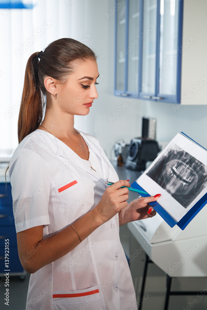 Woman Dentist examines x-ray of his pen in his hand. On the x- ray picture shows the teeth.