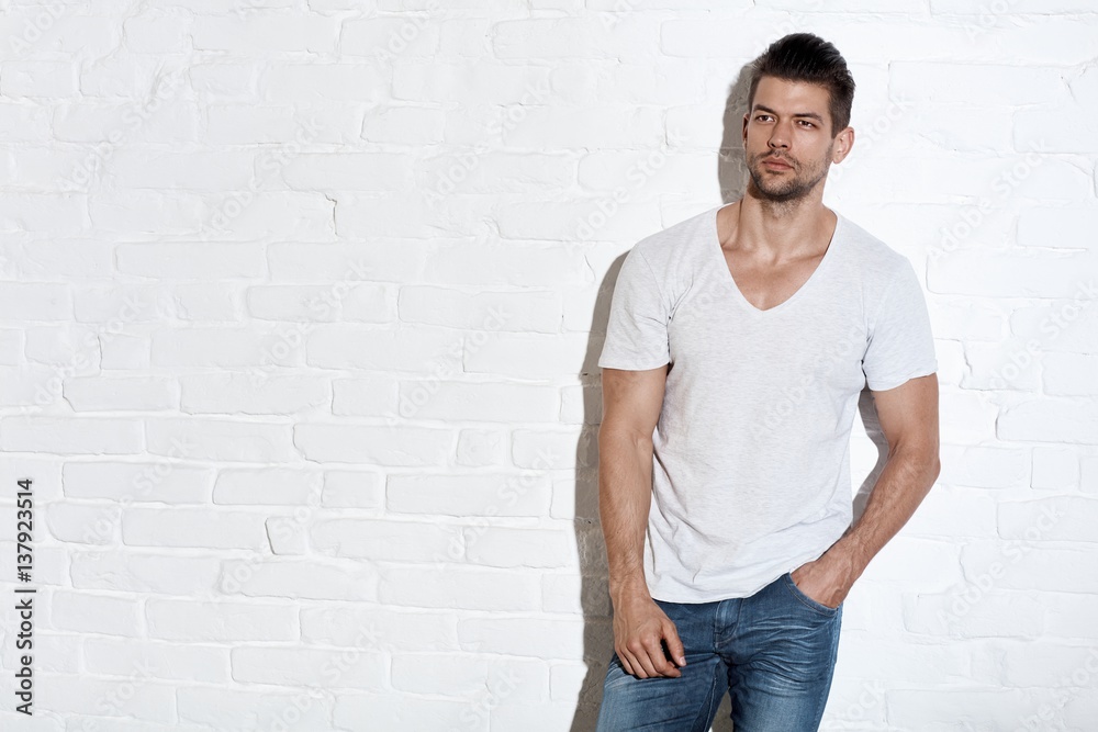 Serious young man standing at white brick wall Serious young man standing at white brick wall
