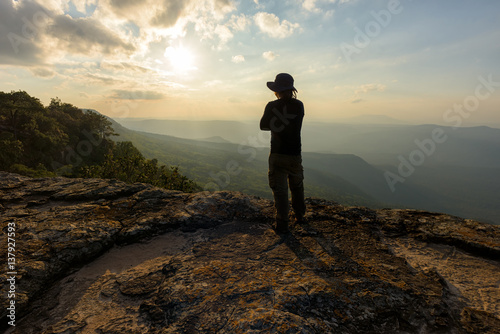 Man on the top of a rock to face the sunset - success concept