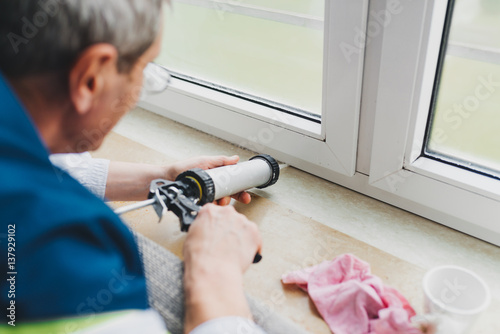 Backview of old man using a silicone tube  for repairing the window