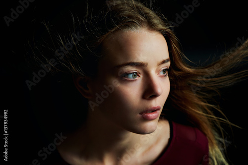 Beautiful girl looking to the side, in profile, Hair flying. Drama. Studio photography in low key on a background