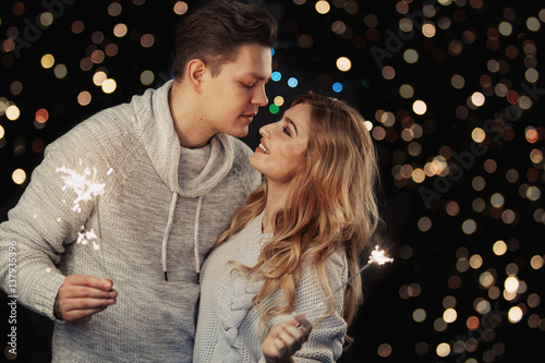 Cheerful couple in winter clothes hugging and kissing. Low light