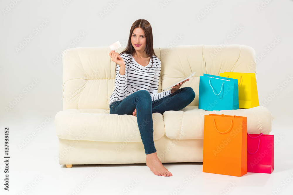 Young woman with credit card buying sitting on sofa with paper bags and new clothes Young woman with credit card buying sitting on sofa with paper bags and new clothes