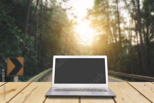 Laptop with blank screen on wooden table with dark misty forest