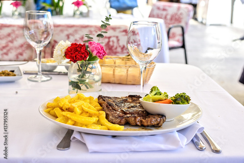 Grilled steak with french fries and vegetables on a white table outdoors. Fresh served