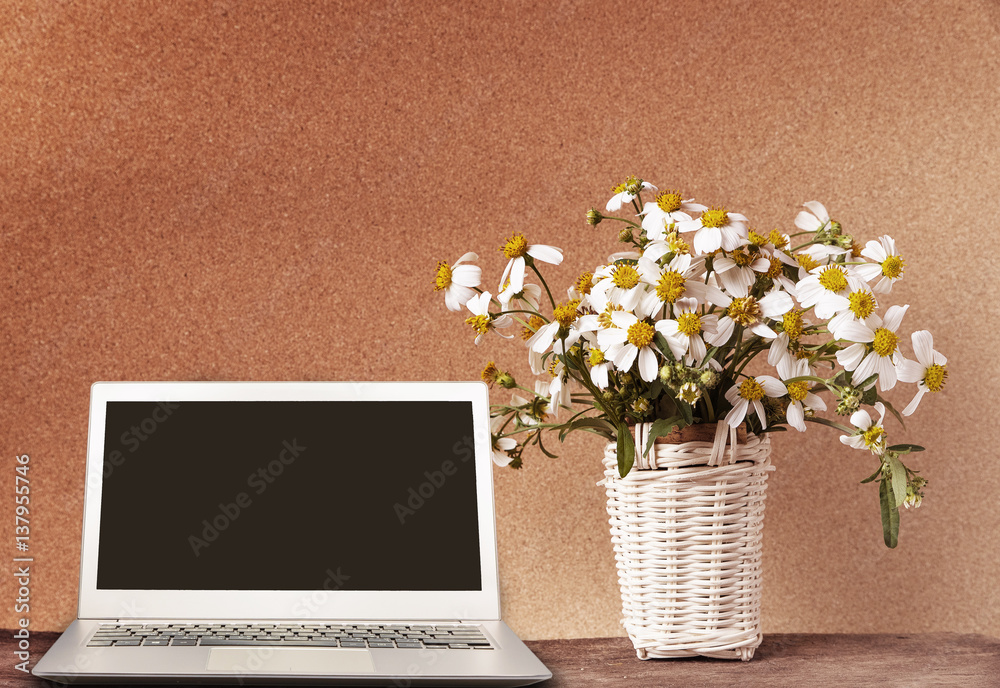 Laptop with blank screen on wooden table with basket of chamomile flower