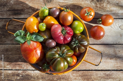 Various types of tomatoes in an orange, enamel sieve on a wooden surface photo