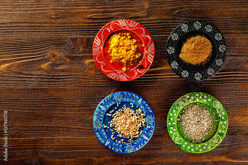 Closeup image of colorful ethnic style plates with spices at wooden table background.