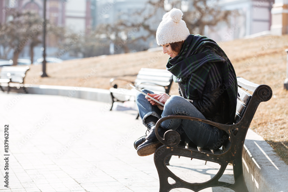 Happy woman sitting and using tablet outdoors in the city