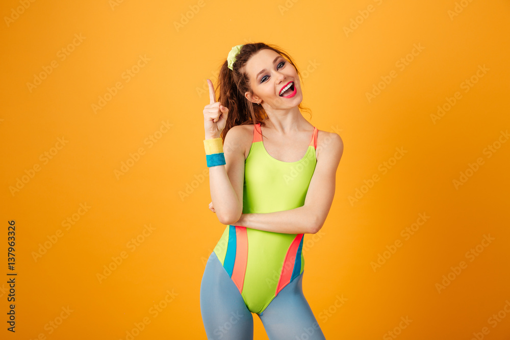 Smiling cute young woman athlete standing and pointing up Smiling cute young woman athlete standing and pointing up
