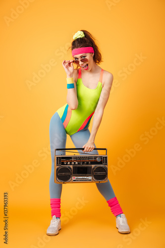 Smiling playful young woman athlete in sunglasses holding retro boombox