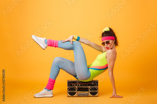 Fototapeta Naklejka Na Ścianę i Meble -  Playful young woman athlete sitting on retro boombox and posing