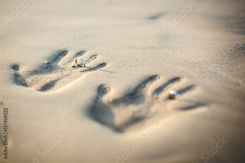 Couple of lovers at a beautiful sunset over the ocean. Couple on a romantic vacation. Imprint pair of hands in the sand, wedding ring.