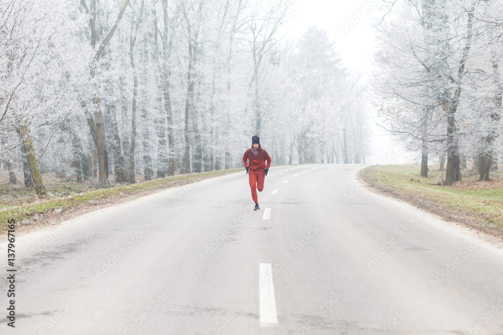 Young athletic man running on the road in winter.