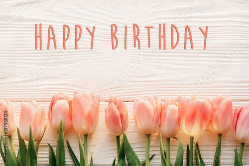 Photo happy birthday text sign on pink tulips on white rustic wooden background flat lay