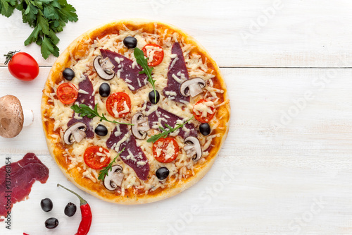 Fototapeta Naklejka Na Ścianę i Meble -  fresh pizza in a rustic Italian style with jerky olives mushrooms and three kinds of cheese on a light wooden background
