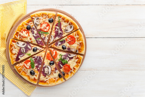 fresh pizza in a rustic Italian style with jerky olives mushrooms and three kinds of cheese on a light wooden background