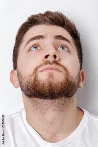 portrait of handsome young thinking man with beard looks up on w