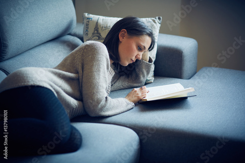 Ragazza legge libro sul divano a casa photo