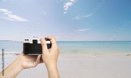 Man holding film camera ready to take photo over sea beach with blue sky background