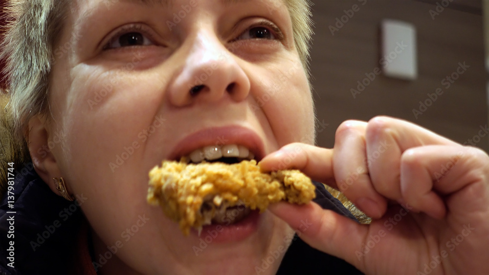 Woman expressively eats chicken in fast food restaurant. Face closeup shot. Woman expressively eats chicken in fast food restaurant. Face closeup shot.