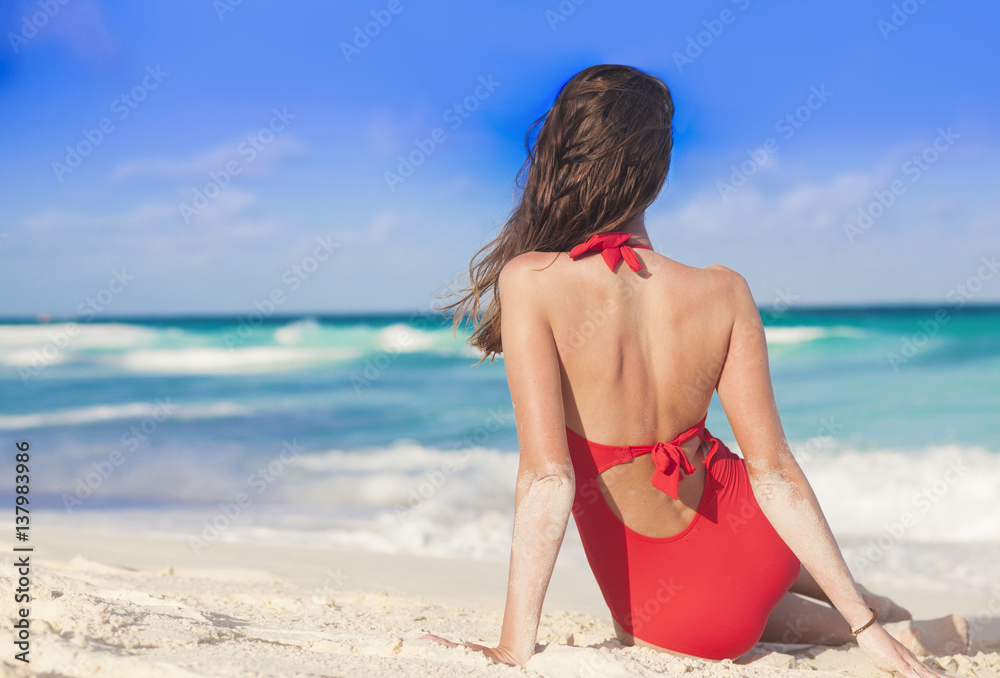 back view of woman in bikini relaxing at white sand beach