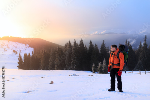 Hiker in winter mountains. Man with backpack trekking in mountains. Winter hiking. Beautiful sunrise in the winter mountains. © Serhii