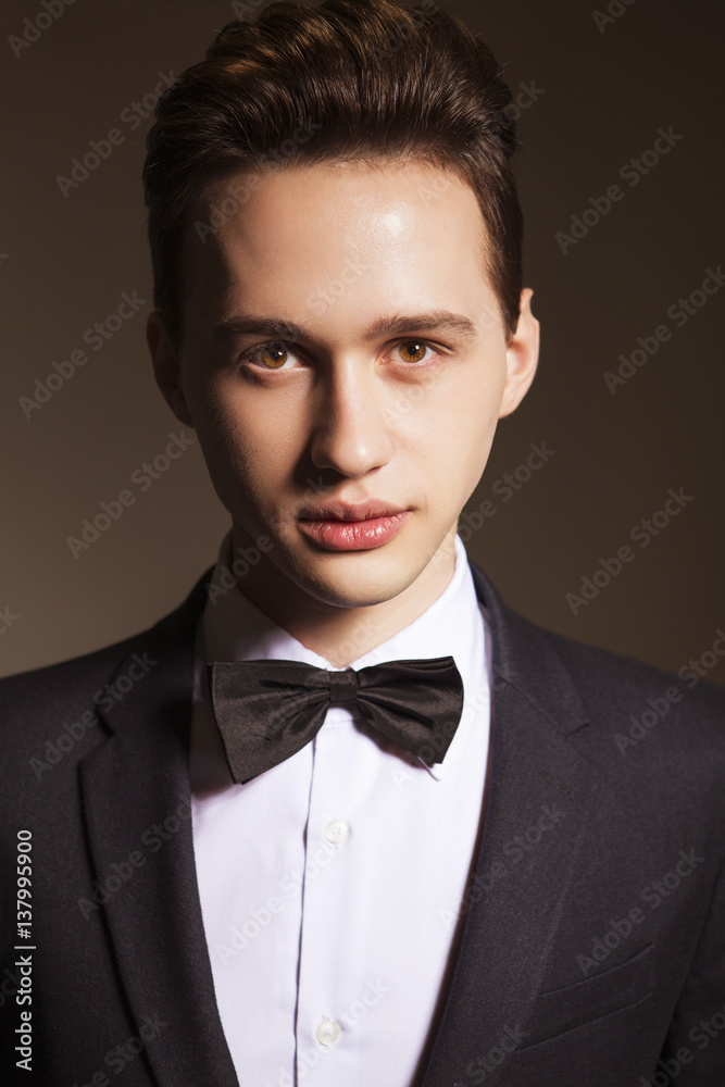 Young handsome brunette macho businessman in black suit and bow tie. neutral background Young handsome brunette macho businessman in black suit and bow tie. neutral background