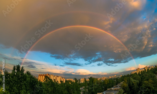 Evening rainbow in the sky over the city at sunset in the summer, in the rain