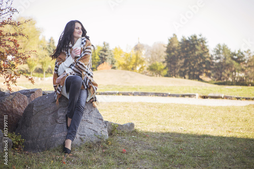 Beautiful caucasian brunette young woman in warm autumn day at park. Yellow leaves and sunshine. Fall season. Woman in white sweater and plaid with a cup of coffee in hands, smiling. Copy space © AnnaDemy